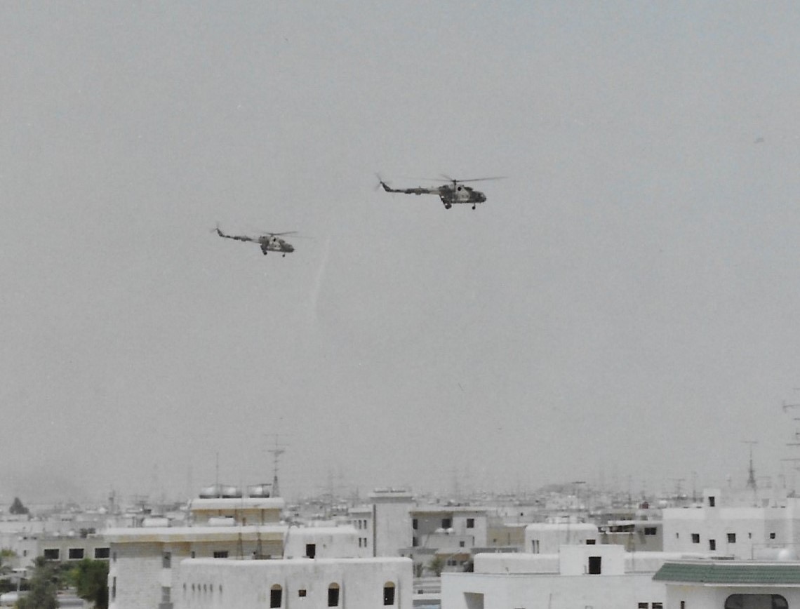 Black and white image shows two helicopters flying over village in Kuwait.